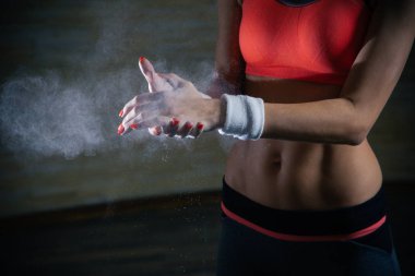 Sportif kıyafetler içinde duran ve ellerine talk pudrası uygulayan kırmızı tırnaklı genç kadının yakın çekim