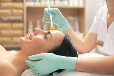 Beyaz havlu ve yüzünde soyma iletken lastik eldiven güzellik elleri üzerinde yatan pozitif genç koyu saçlı kadın