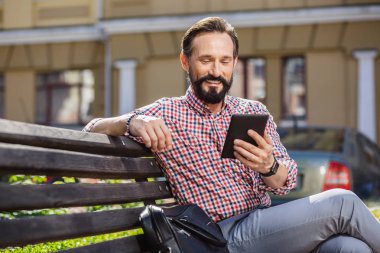 Modern bir cihaz. E-kitap okurken neşeli yakışıklı adam açık havada oturan