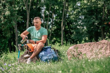 Ağaç kütüğünde otururken serinletici bir içecek içen protezli hoş genç adam