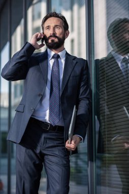 Ciddi bir tavır. Telefonda konuşurken cam duvara yaslanmış kendine güvenen bir işadamı