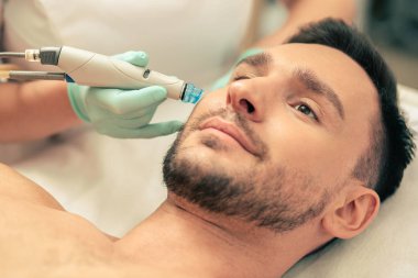 Cilt besleyici işlem sırasında yüzünün yanında modern bir araç tutan lastik eldiven ve el görünümlü adam yakın
