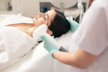 Gözleri kapalı modern klinikte lazer tedavisi gören sakin bayanın yan görünümü