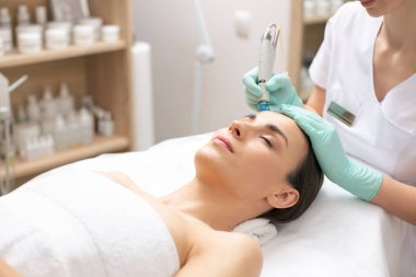 Profesyonel kozmetolojist yüzünde dermabrazyon işlemi yaparken gözleri kapalı sakin genç kadın