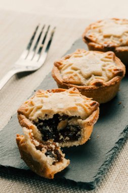 Üzerinde üç yaban mersini kıyma turta ile siyah bir kayrak dikdörtgen fotoğraf kapatın. Kayrak yakınındaki arka planda çatal