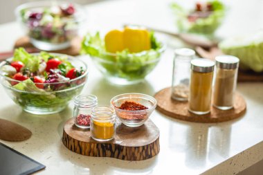 Sebze kase yanında duran cam kase lezzetli taze salata. Ön planda küçük kase ve şişelerde Baharatlar