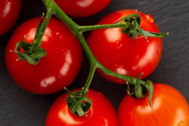 Koyu gri yüzeye yerleştirilen yeşil ıslak dal üzerinde olgun kırmızı kiraz domates yakın