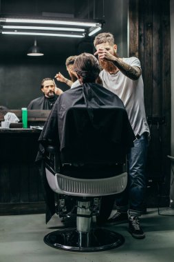 Konsantre profesyonel berber onun saç modeli nde çalışırken kuaför elbisesi içinde müvekkilinin yanında duran