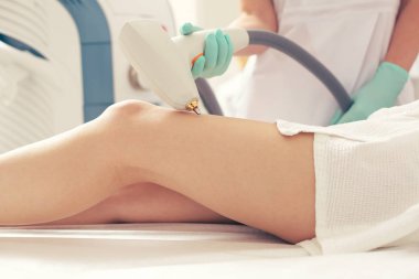 Hastanın bacağı yakınında modern bir aparat tutan ve vasküler ağların çıkarılması için kullanan kauçuk eldivenelin fotoğrafına yakın