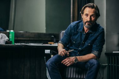 Modern berber dükkanında iken makası tutan kot pantolon elbiseli sakallı ciddi adam