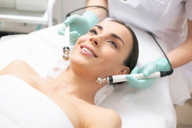 Duygusal genç kadın mikrocurrent tedavi sırasında tıbbi kanepede yatarken kendinden emin ve gülümseyen görünümlü