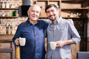 Birlikte mutlu. Neşeli yaşlı baba ve oğlu evde kahve içerken kucaklayan