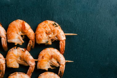 Siyah kayrak yüzeyinde sıralar halinde yatan ahşap kazmalezzetli kızarmış karidesler