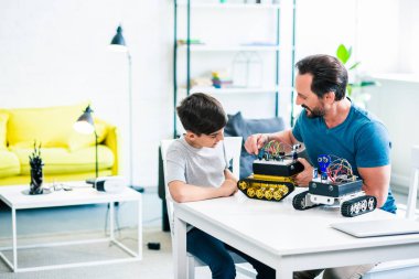 Neşeli baba ve oğul robotik cihazlarını yaparken masada oturuyorlar.