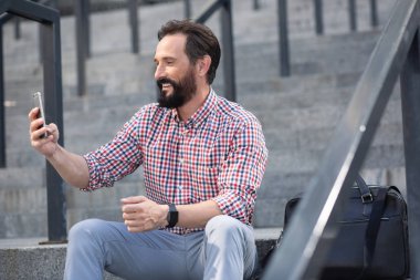Açık havada merdivenlerde otururken telefonunu kullanan yakışıklı pozitif adam