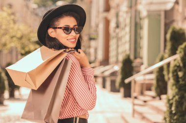 Omzuna alışveriş çantaları koyarak güneş gözlüğü ve şapka mutlu genç kadın