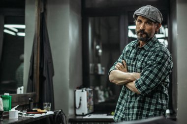 Sakin çekici sakallı adam kollarını çapraz ayakta ve berber dükkanında ayakta iken size bakıyor