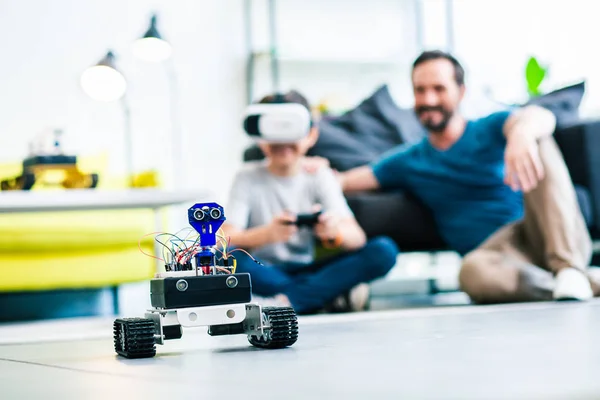 一个小机器人在地板上的选择性焦点与父亲和儿子坐在背景 — 图库照片