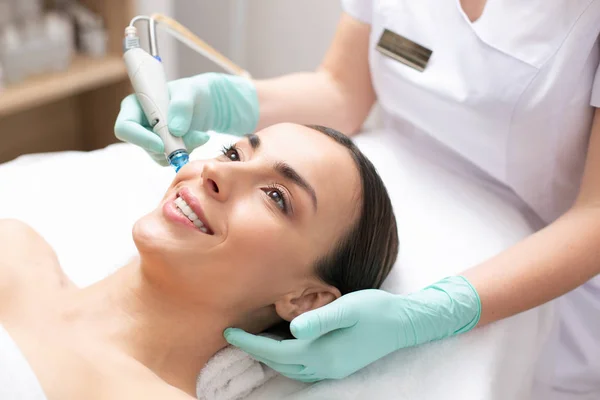 Jovem Alegre Sorrindo Enquanto Cosmetologista Profissional Limpando Poros Sua Pele — Fotografia de Stock