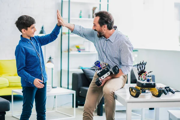 积极慈爱的父亲给儿子高五 同时拿着一个机器人设备 — 图库照片