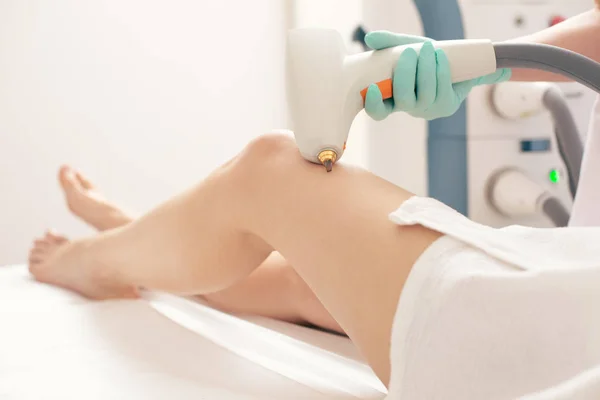 Close up photo of the legs of woman and professional medical worker holding a modern apparatus while removing vascular nets