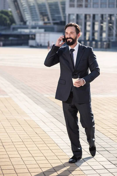 Get in touch. Cheerful handsoem businessman walking to work while having a conversation on phone