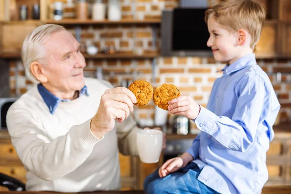 美味的饼干 愉快的小男孩吃回家做糕点与他的祖父 而休息在家里 — 图库照片