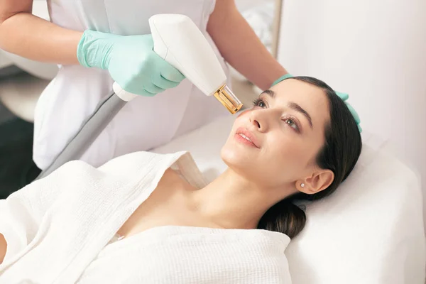 Pretty young lady lying on the medical couch and looking confident while undergoing the procedure of laser removal of stretch marks on her face