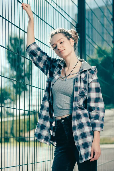 Calm peaceful young lady looking relaxed and thoughtfully looking down while standing near the chain link fence