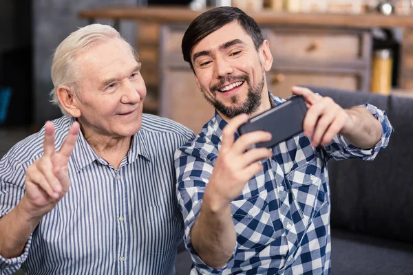 真正的幸福欢快的微笑老人在镜头前摆姿势 同时与他的儿子自拍 — 图库照片