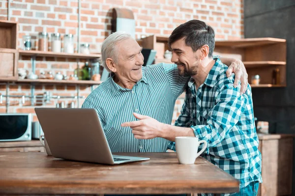 温暖的关系 快乐善良的老人微笑着拥抱他的儿子 同时学习如何使用笔记本电脑 — 图库照片