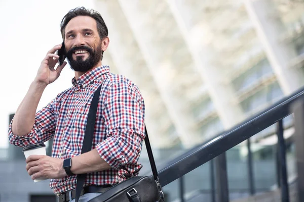 Glad to talk to you. Overjoyed pleasant man smiling while talking on phone outdoors