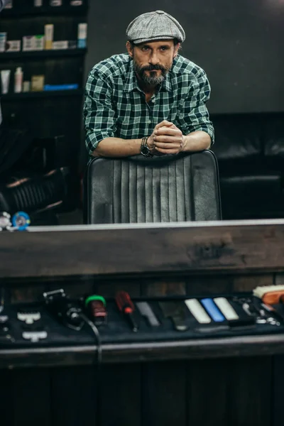 Attractive Bearded Man Flat Cap Standing Barbershop Putting Hands Armchair — Stock Photo, Image