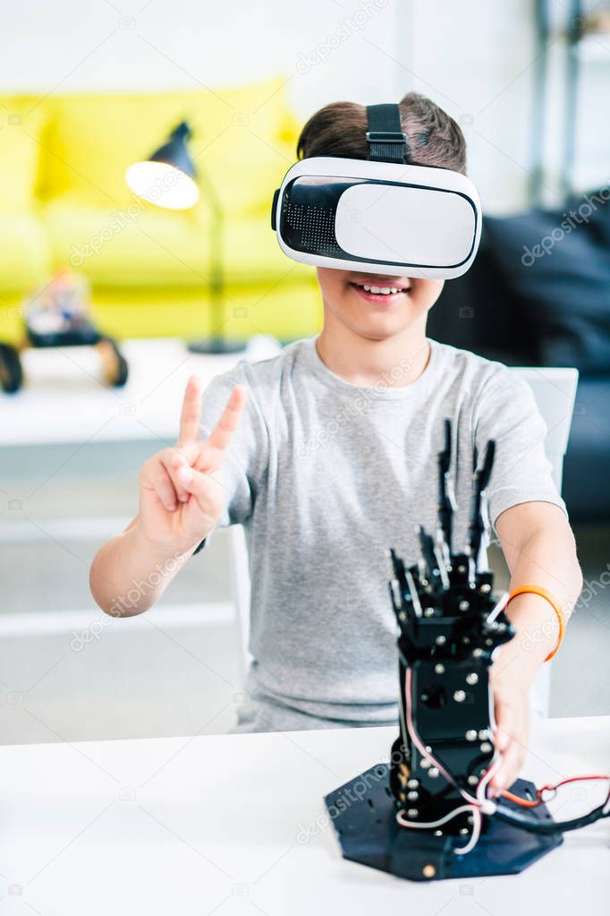 Cheerful little smart boy using his VR glasses while experimenting with humanoid robotic hand at home