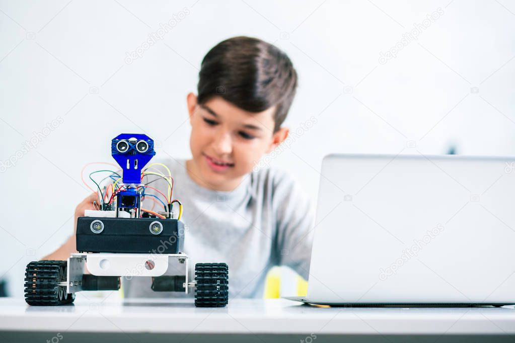 Selective focus of a modern robot standing on the table while a little enthusiastic boy testing it