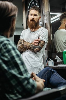 Sakin sakallı berber dövmeli kolları ile ayakta geçti ve onu dinlerken ziyaretçidikkatle bakıyor