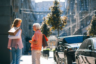 Gladsome kadın ve annesi kağıt torba taşıyan ve birbirlerine açık havada gülümseyerek