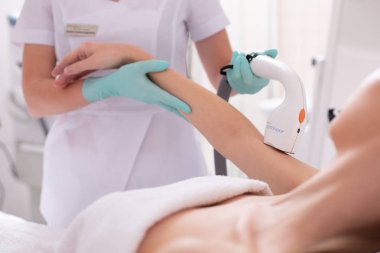 Profesyonel güzellik uzmanı kadının elini tutarken ve kolunda lazer epilasyon yaparken lastik eldiven giyiyor