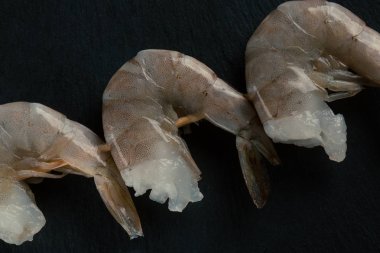 Üzerinde başsız ham karides ile siyah yüzeyüzerinde şiş fotoğrafı yakın