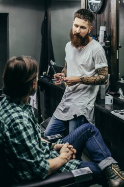 Sakin genç şık berber müvekkilinin önünde oturan ve tarak tutarken ona bakıyor