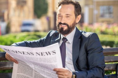 İş konsepti. Kürsüde dinlenirken gazete okuyan neşeli bir profesyonel işadamının portresi