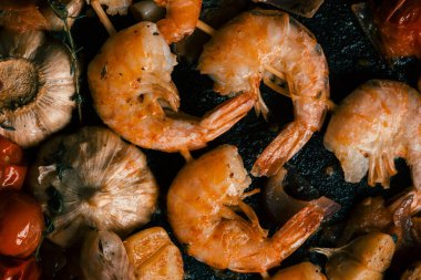 Haşlanmış sarımsak soğanı ve kiraz domates ile tavada yatan gevrek kabuklu yağlı karidesler