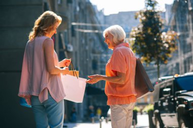 Mutlu yaşlı kadın gülümseyen ve alışveriş çantaları ile yetişkin kızı bakıyor