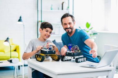 Neşeli küçük oğlu ve babası masada oturan ve evde robotları test
