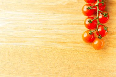 Ahşap yüzeyüzerinde yatarken temiz ve taze görünümlü kiraz domates dalı bölümünün üst görünümü. Sol taraftaki alanı kopyalama