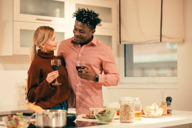 Güzel romantik genç çift ellerinde şarap kadehleri ile mutfakta ayakta ve birbirlerine gülümseyerek