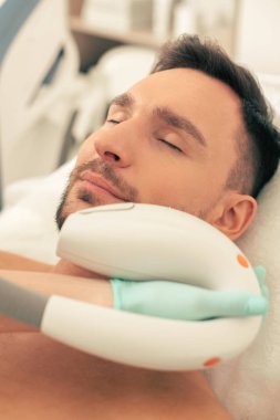 Gözlerini kapatan ve güzellik uzmanının fotoğraf gençleştirme işlemini gerçekleştiren koyu saçlı adamın yakın fotoğrafı