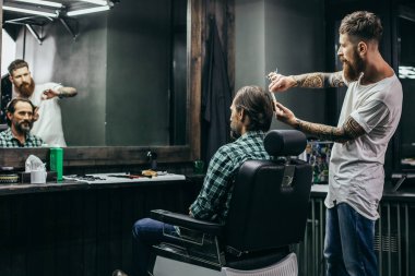 Careful professional barber standing behind the back of his client and doing haircut for him