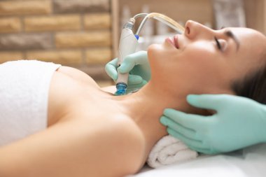 Genç memnun müşteri cilt üzerinde dermabrazyon prosedürü yürüten profesyonel kozmetolojist