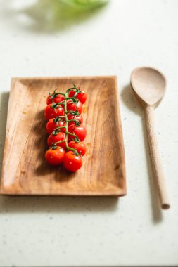 Yanında tahta kaşıkla tahta dikdörtgen tabakta kiraz domates dalı kapatın